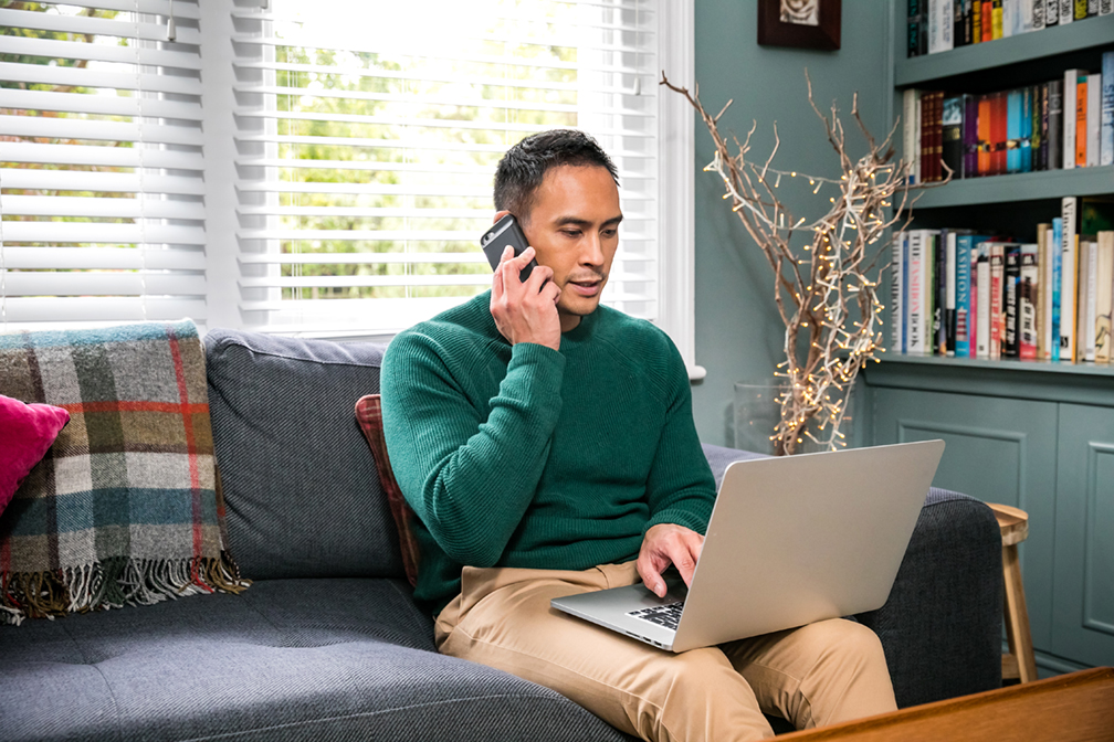 Customer on couch on the phone and looking at laptop