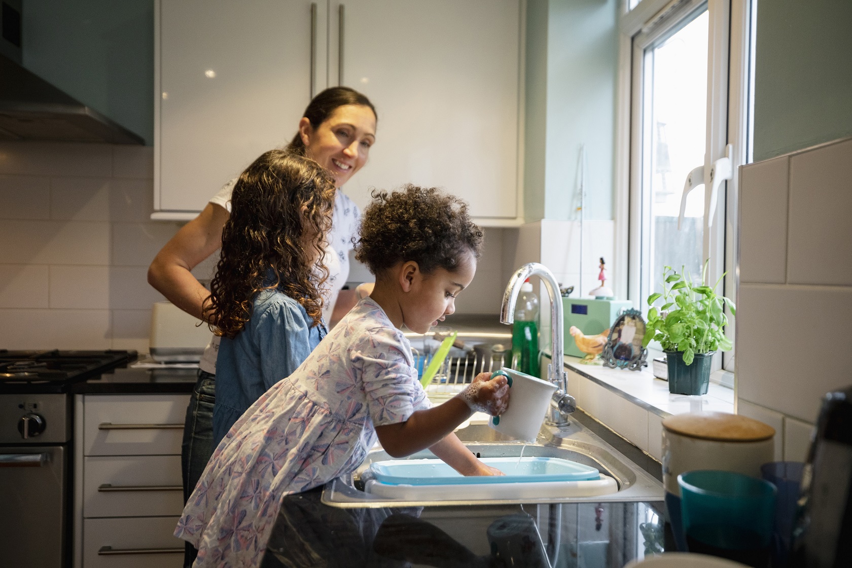 Two children help their mum with the washing up using a washing up bowl